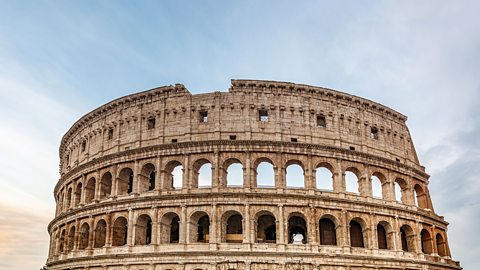 The ruins of the curved wall of the Colosseum in Rome, with many levels of curved archways through which the sky is visible.