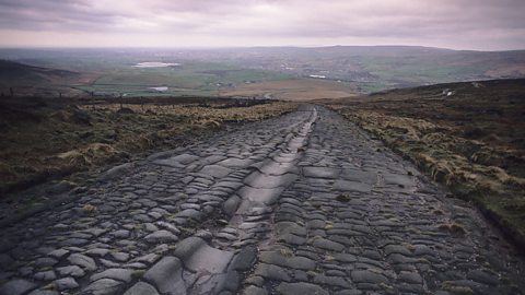 In the countryside, a straight paved road stretches down from the hills into the distance