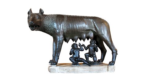 Two children, Romulus and Remus, kneel beneath a wolf, ready to feed from her teats