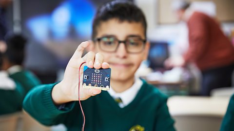 A primary school child holds a micro:bit displaying a smiley face