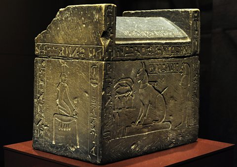 A sarcophagus with a carving that shows a cat sitting by an offering table 