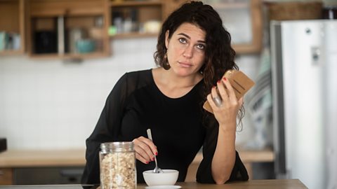 A woman looks unimpressed while eating and looking at her phone