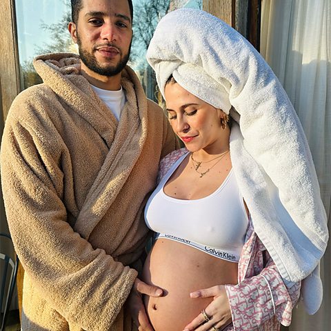 Suzie Bakos and her partner Daniel Sylvester Woolford from People Just Do Nothing pose for a picture with her baby bump. He is wearing a dressing gown and she has a hair towel on.