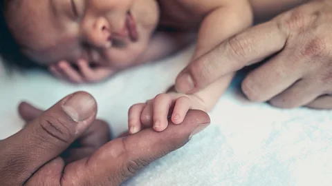 Getty Images A baby with two adult hands touching (Credit: Getty Images)