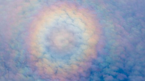 A sky of clouds with a full rainbow above taken from the view of an aeroplane.