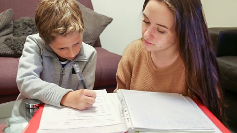 A teenager helps a younger child with their homework