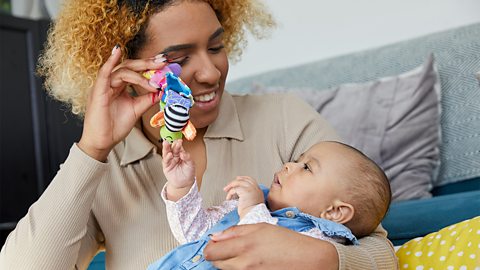 A mum and her young baby playing with a colourful toy.