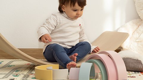 A toddler playing with pastel coloured rainbow toys.