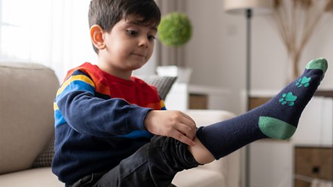 A little boy pulling on a sock.