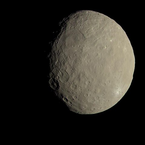 An image of ceres, showing a bumpy crater marked surface in a green grey colour