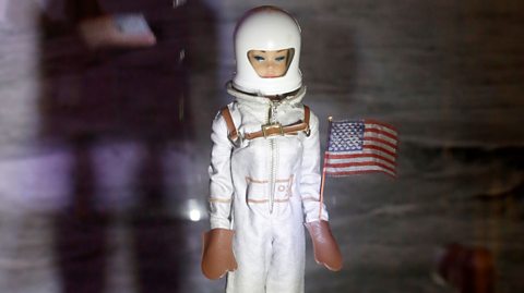 Miss Astronaut Barbie with a miniature American flag.