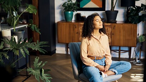 A woman with dark curly hair sitting in a chair looking peaceful with her eyes closed.