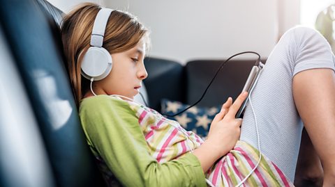 A young girl, with headphones on, playing on her tablet