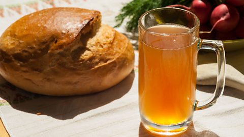 A tall glass of yellow drink next to a loaf of crusty bread, on a table.