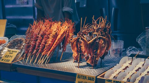 A food stall displaying several skewers of deep-fried squid.