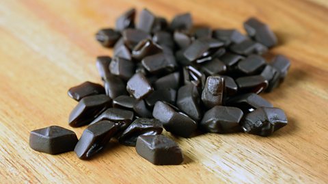 A handful of black liquorice pieces on a wooden table.