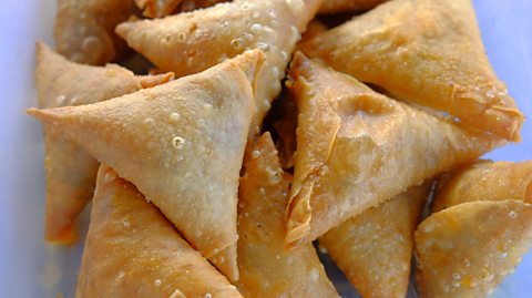 Samosas, deep-friend triangles of pastry filled with vegetables and spices, on a white background.