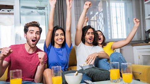 Group of friends sit with glasses of orange juice watching a football game