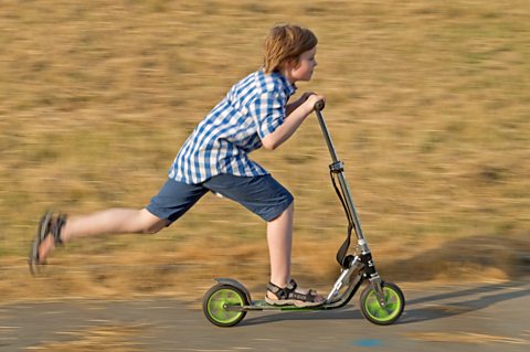 A boy on a scooter pushes himself along using his foot.