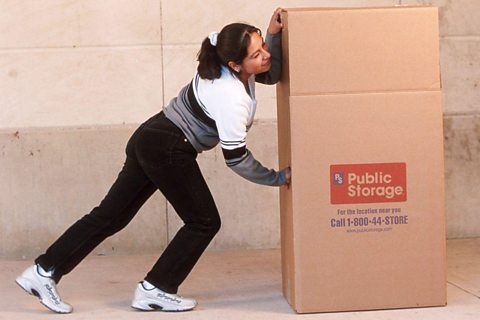 A girl pushes a large cardboard box.