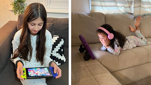 Two girls sat on a sofa. One is playing a game on her device and one is watching a film.