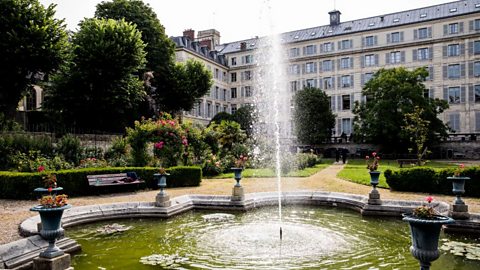 A general view of L'Institut National de Jeunes Sourds de Paris, a grey building with a fountain and trees in front of it.