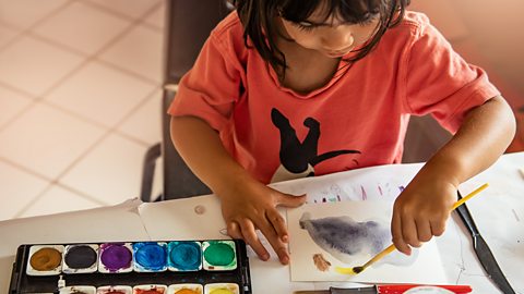 A 2 1/2 year old toddler girl paining with water colors using her left hand.