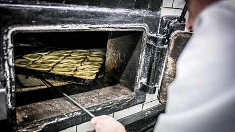M. Manze Baker pulling a tray of eel pies of out an oven