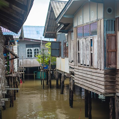 Pnotograph showing wooden houses on stilts overhanging a river of brown water.