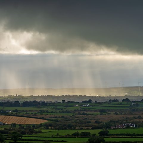 Photograph showing sun shining through a cloudy grey sky over County Antrim.