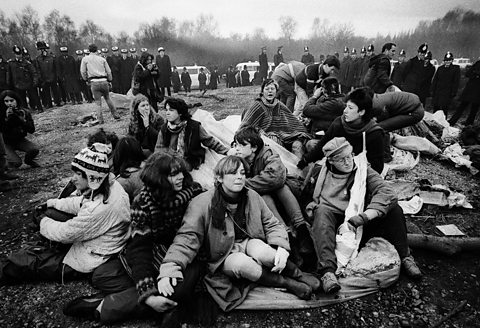 Ffotograff o grŵp o ferched yn protestio yn Greenham Common wedi’u hamgylchynnu gan swyddogion yr heddlu.