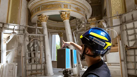 Getty Images A Unesco consultant in a hard hat films a cathedral damaged by war