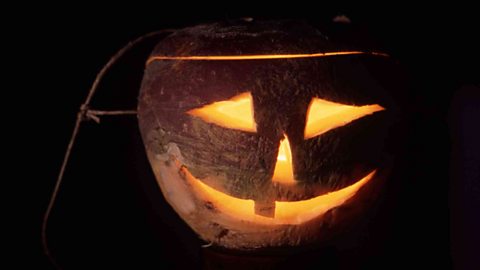 Halloween lantern made from a carved out turnip with glowing eyes, nose and mouth lit by candle inside.