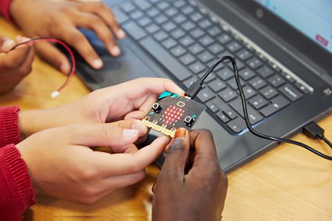 Primary school children holding a micro:bit displaying a heart