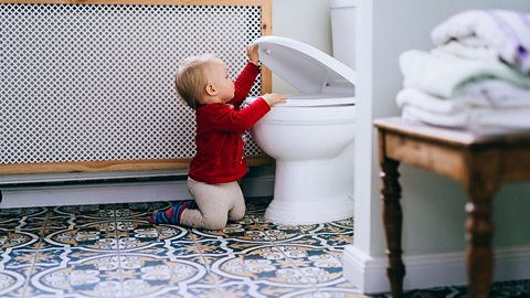 Little baby girl looking into toilet in a bathroom. - stock photo