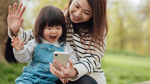 A mum and her daughter on a video call in a park.