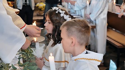 Two children, a boy and a girl, dressed in white gowns, hold candles during their first communion in a Catholic church in Lyadsk, Belarus in May 2021.