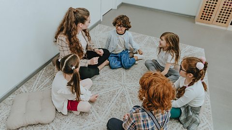 Schoolchildren with their teacher sitting on the floor in circle in a classroom. Elementary students classmates discussing something with each other.