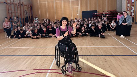 Abby Cook holds up micro:bit in front of primary school pupils in school assembly hall