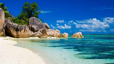 A beach with white sand and rocks with blue sky in the background.