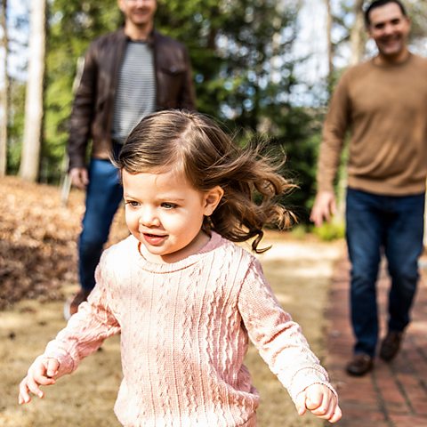 Gay couple walking with toddler daughter in front of their home - stock photo