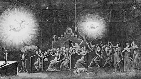 An etching of phantasmagoria theatre projections of a demon and a flying skull, hovering above a cowering audoence of people.