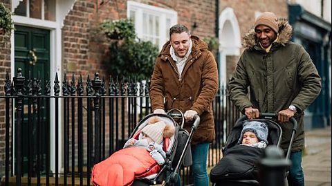 Two fathers pushing prams and chatting.