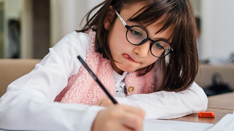 Young girl in glasses concentrates on writing a story at her kitchen table