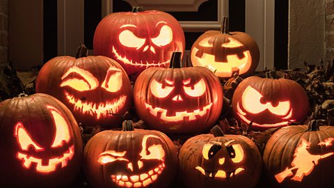 A pile of lit up carved pumpkins with various spooky faces on them.