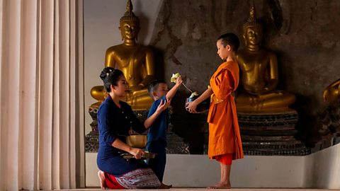 A mother and child making an offering to a boy monk at a temple in Thailand.