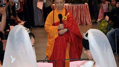 A Buddhist wedding ceremony with two women in the foreground and a Buddhist monk officiating.