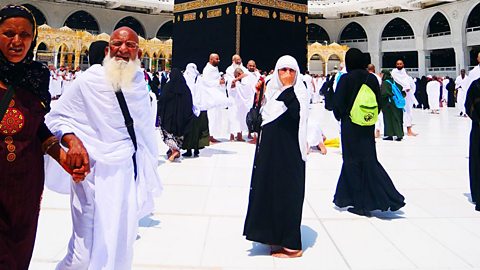 Two Muslim women with a Muslim man between them face the camera during a Hajj. The woman on the left is holding hands with the man.