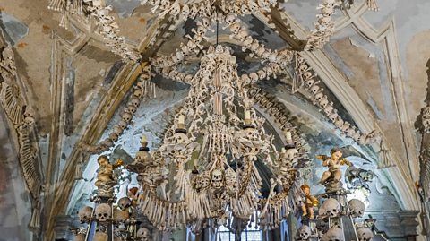 A chandelier made completely of human remains, with garlands of skulls and bones draped above it.