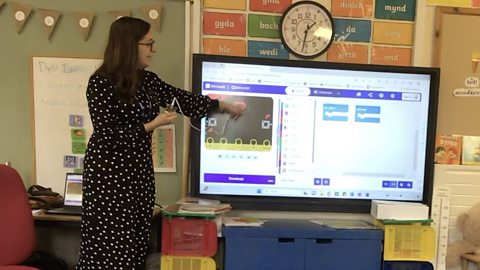 Primary school teachers points at a screen showing the MakeCode coding platform